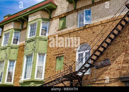 The brightly-lit wall of a small apartment building features vibrant colouring along its brick wall and windows, though the paint peels. Stock Photo