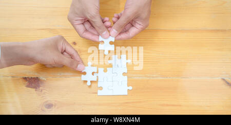 Top view of hands of diverse people assembling jigsaw puzzle together represents teamwork of the group Stock Photo