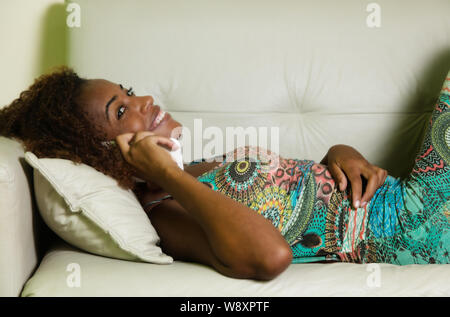 Laughing african american woman speaking at phone on sofa at home in living room Stock Photo