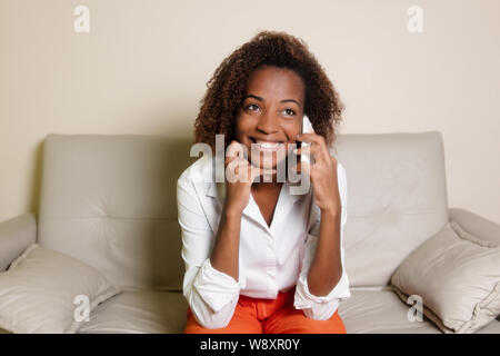 Beautiful african american woman laughing at phone on couch Stock Photo