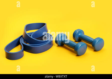 light weight dumbbells and a blue exercise resistance band on a bright yellow background . Stock Photo