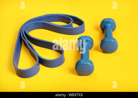 light weight dumbbells and a blue exercise resistance band on a bright yellow background . Stock Photo
