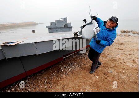 80-year-old Wen Yuzhu takes off a model of the J-20 stealth fighter from his homemade model of Chinas first aircraft carrier The Liaoning on a beach i Stock Photo