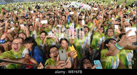 Volunteers use their smartphones to take selfies during a farewell party in the Nanjing Olympic Sports Center Stadium during the 2014 Summer Youth Oly Stock Photo