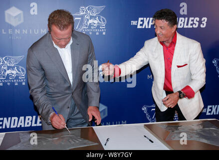 American actors Arnold Schwarzenegger, left, and Sylvester Stallone signs their names after leaving their handprints at the premiere of their movie, T