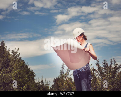 Young, cute woman holding paper project in the park against the backdrop of green trees. Close-up. Concept of labor and employment Stock Photo