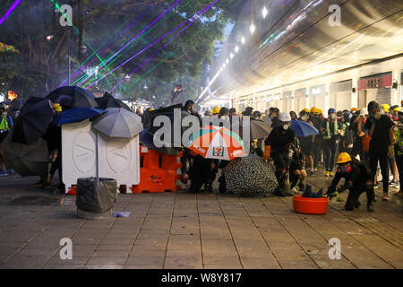 11th August 2019 Hong Kong. Protesters taking cover behind barricades and umbrellas as police fire tear gas and rubber bullets from Tsim Sha Tsui Police Station during an anti extradition bill protest. Stock Photo