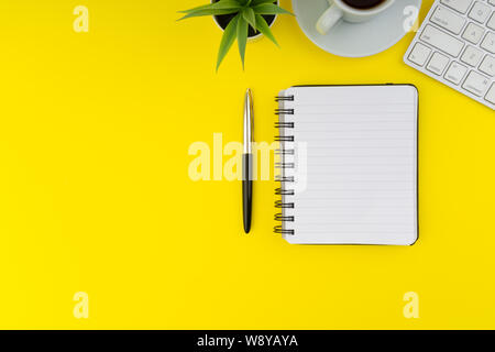 Flat lay view of office table desk. Workspace with keyboard, pen, book, coffee and decoration flower on yellow background. Copy Space concept Stock Photo