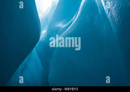 Detail shot from deep within a crevasse or ice cave on the Matanuska Glacier in Alaska. Close up of light reflecting off curving ice wall underground. Stock Photo