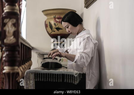 35-year-old Yang Xiaoting plays guqin, a plucked seven-string Chinese musical instrument, at her embroidery studio in Wuhan city, central China's Hube Stock Photo