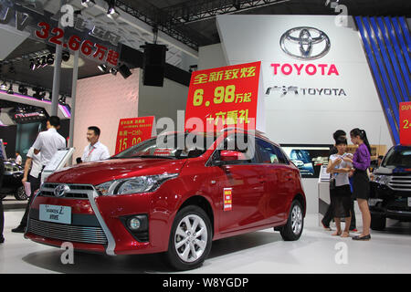 --FILE--Employees are seen next to a Toyota Yaris L during an automobile exhibition in Haikou city, south Chinas Hainan province, 12 July 2014.   Toyo Stock Photo