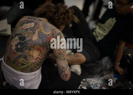 Japanese tattoo artist Horitsuna, left, shows the tattoo on his back while inking a customer during the Second International Hong Kong Tattoo Conventi Stock Photo