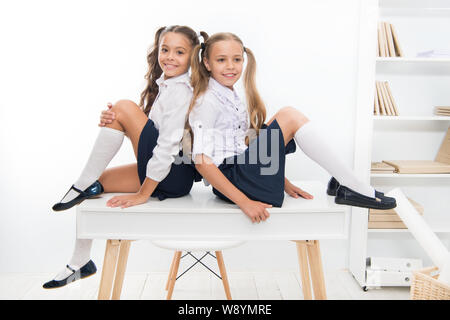 Schoolgirls friends sit on desk. Best friends relaxing. Schoolgirls tidy hairstyle relaxing having rest. School uniform. Rebellious spirit. School club. Little schoolgirls classmates friendly kids. Stock Photo