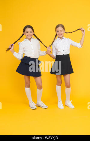 Perfect hairstyle for perfect schoolgirls. Adorable small girls with long hairstyle on yellow background. Cute little children holding braided hairstyle. Getting your hairstyle to last all day. Stock Photo
