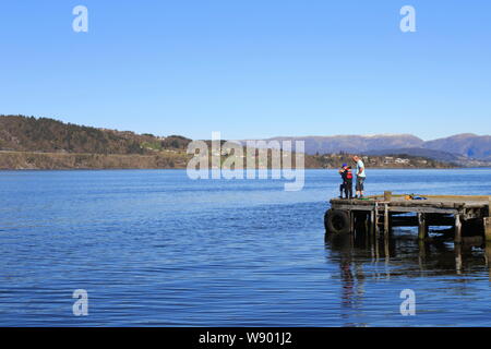 A man and two children fish in the fjord from a jetty on the island of Osterøy in Hordaland county, Norway, during the spring. Stock Photo