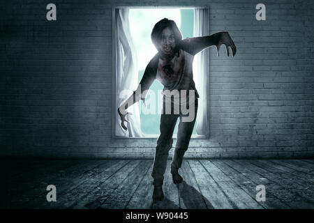 Scary zombie with blood and wound on his body standing in the abandoned ...