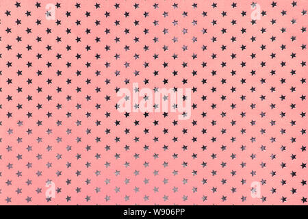 Pink background from metal foil paper with a pattern of sparkling silver stars, closeup. Texture of rose metallized wrapping holiday paper surface. Stock Photo
