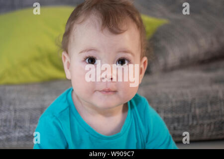 Portrait of a cute surprised toddler girl boy of 10 months. Baby looks with surprised eyes. A child in a blue shirt, a large portrait of a funny surpr Stock Photo