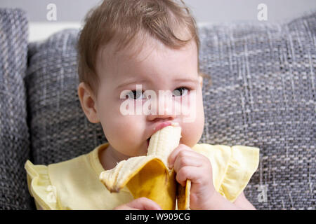 The child eats a banana. Portrait of a little baby girl close-up. Girl cleans a banana and eats pulp Caucasian Caucasian Brown Eyes Baby Eating Fruits Stock Photo