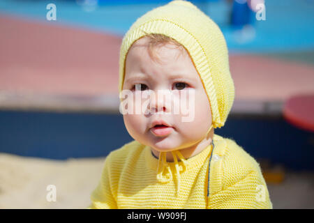 Face baby girl boy 1 year old portrait close-up. The child in a yellow knit hat outdoors Stock Photo