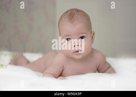 Cute newborn baby boy girl lies on the bed and carefully looks into the camera. European baby kid learns to keep his head on his own, soft focus Stock Photo