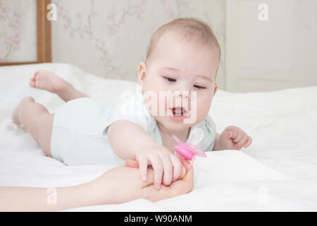 The six-month-old baby girl lies on her stomach and pulls her hand to the nipple. A small child in white looks at the pacifier opened his mouth. Portr Stock Photo