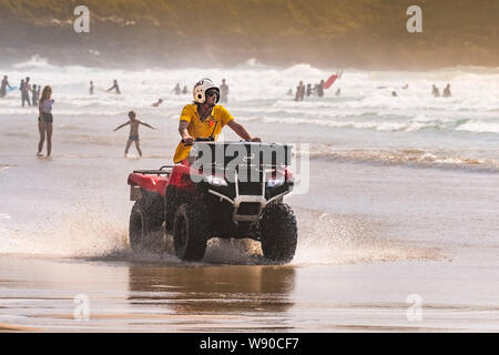 A RNLI Lifeguard riding a quadbike and patrolling along the shoreline at Fistral Beach in Newquay in Cornwall. Stock Photo