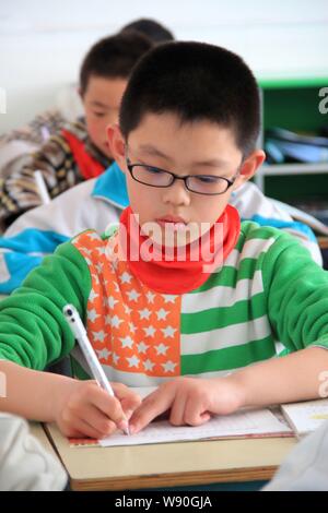 --FILE--A young near-sighted Chinese student wearing glasses writes during a class at a primary school in Wendeng city, east China's Shandong province Stock Photo