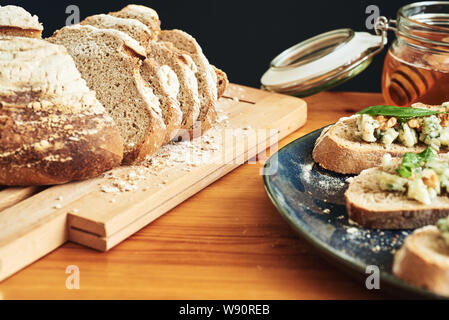 Close up on a plate of toasts with roquefort cheese, walnuts, honey and basil. Some bread and honey in the background Stock Photo