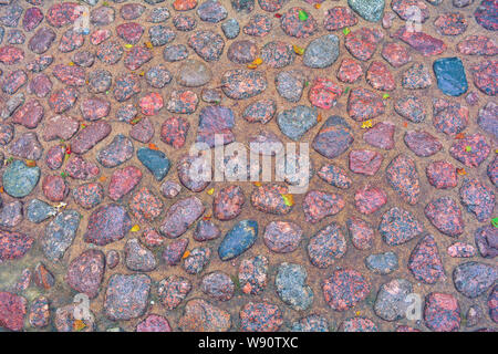Stone background of pavement with rough wet granite boulders. Texture of historic medieval cobble paving is laid on the city street Stock Photo