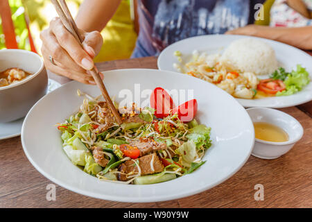 Hands with chopsticks, eating Yam Nuea Yang or Thai beef salad - traditional cuisine of Thailand. Sauce on the side. On green background. Stock Photo