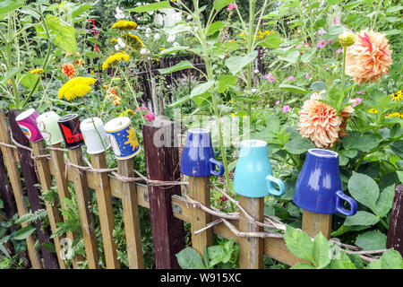 Wooden garden fence in the overgrown garden with colorful mugs on planks, cottage garden Germany Urban garden wooden fence garden Stock Photo