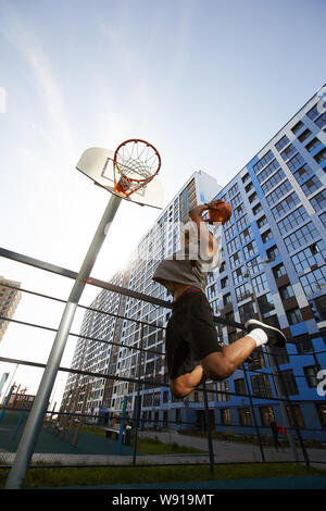 Low angle action shot of African basketball player jumping while shooting slam dunk in outdoor court, copy space