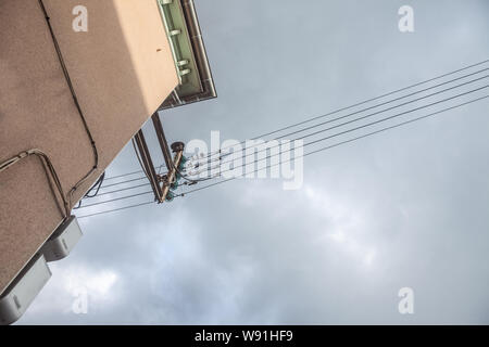 Obsolete old electrical power lines, with their vintage isolators, abiding by former industrial European standards, on a old building in a French vill Stock Photo