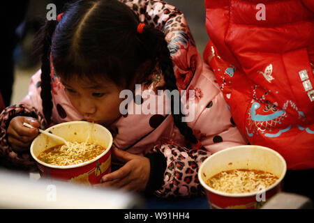 A little girl is eating instant noodles at Wuhan Railway Station as her family prepares to hit the road for home in Wuhan, central Chinas Hubei provin Stock Photo