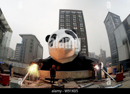 Chinese workers weld steel frames to install a giant panda-shaped art installation on the facade of the Chengdu IFS shopping mall in Chengdu city, sou Stock Photo