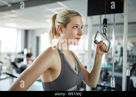 Sporty young woman trains triceps muscle on cable in fitness center Stock Photo