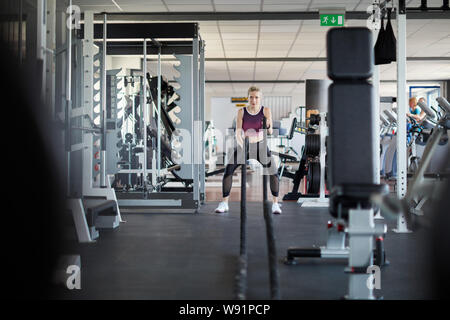 Young woman doing Battle Rope workout for strength endurance in the fitness center Stock Photo