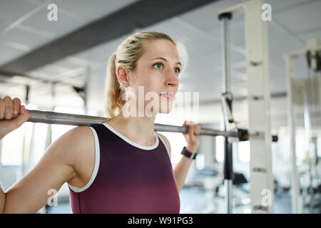 Young woman trains leg muscles in the barbell station in the fitness center Stock Photo