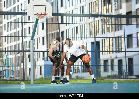 Wide angle action shot of two African-American guys playing basketball in outdoor court in urban setting, copy space Stock Photo