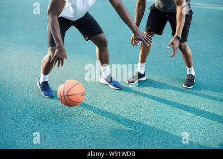Low angle action shot of two African-American guys playing basketball outdoors, copy space