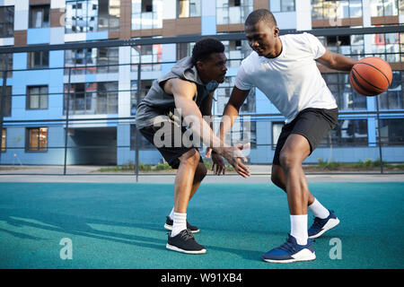 Full length action shot of two muscular African man playing basketball outdoors, copy space Stock Photo