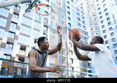 Two sportive African-American men playing basketball in urban setting, copy space Stock Photo