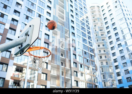 Sports background of basketball ball flying through hoop in urban setting, copy space Stock Photo