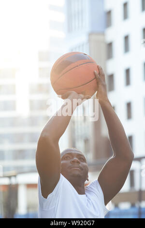 High section portrait of muscular African man throwing basketball ball outdoors, copy space Stock Photo