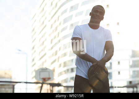 Waist up portrait of handsome African man posing in basketball court outdoors, copy space Stock Photo