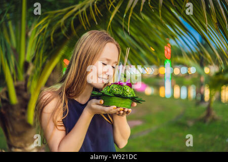 A female tourist holds the Loy Krathong in her hands and is about to launch it into the water. Loy Krathong festival, People buy flowers and candle to Stock Photo