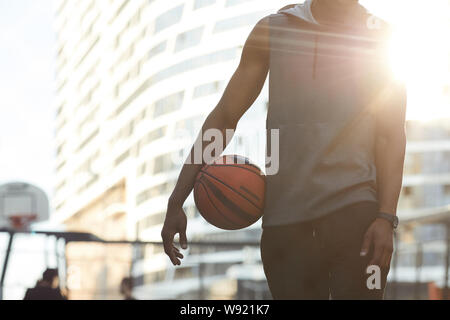 Mid-section portrait of handsome African man holding ball while standing in basketball court outdoors, copy space Stock Photo