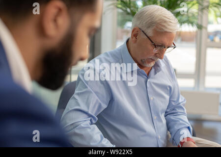 Serious grey-haired male person checking data on document Stock Photo