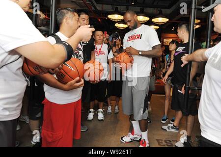 NBA superstar LeBron James, center, signs his signatures on the basketballs to be thrown to a crowd of fans as gifts during a promotional event of Nik Stock Photo